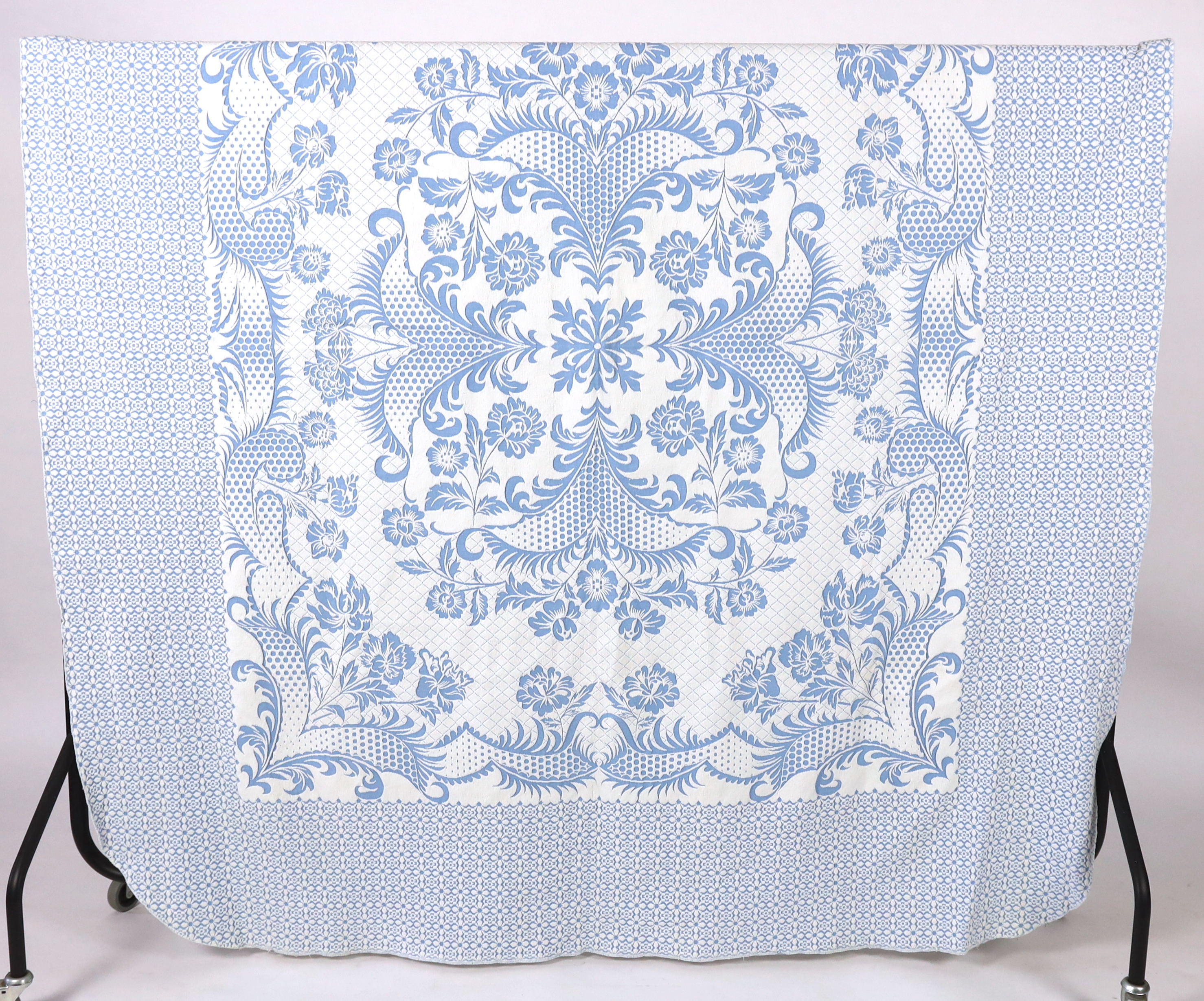 An early 20th century woven 'Marcella' style bed cover, with a blue ground and a white raised floral central cartouche and a wide patterned border, bed cover 194cm wide x 225cm long